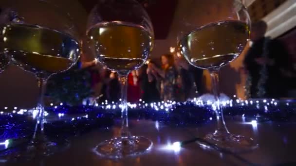 Glasses of champagne on the background of Christmas lights and people who dance at a Christmas party — Stock Video