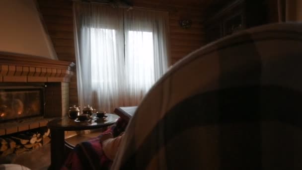 Een bejaarde echtpaar acht een familie foto-album gewikkeld in een deken zitten bij een gezellige open haard. — Stockvideo