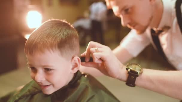 Barbiere fa un taglio di capelli per un piccolo bambino divertente — Video Stock