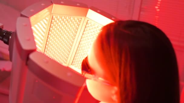 Flickan går igenom en kurs i hudföryngring med hjälp av rött ljus behandling. — Stockvideo