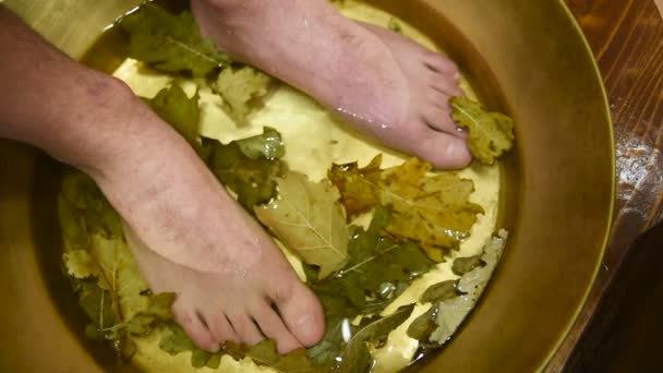 Mens pies en un baño de pedicura con hojas de roble — Vídeo de stock