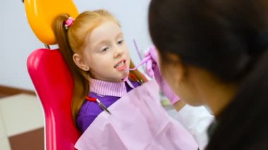 çocuk diş hekimi diş ve ağız küçük, şirin bir kızıl saçlı kızın sarı-kırmızı diş sandalye inceliyor. Pediatrik Diş Hekimliği
