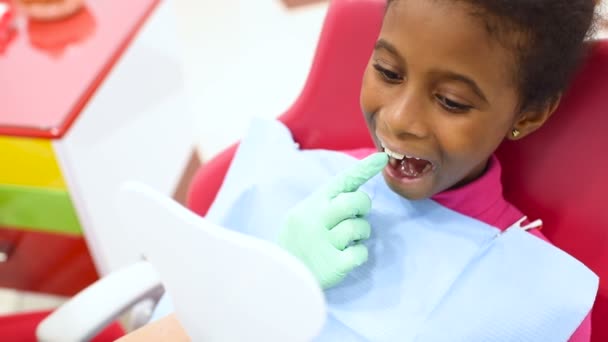 Dětský zubař zkoumá zuby malé roztomilé americkou afričanku v zubařském křesle červené a žluté. — Stock video