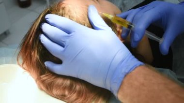 Doktor kozmetolog dermatolog plazmayı hastanın kafa derisine enjekte ediyor..