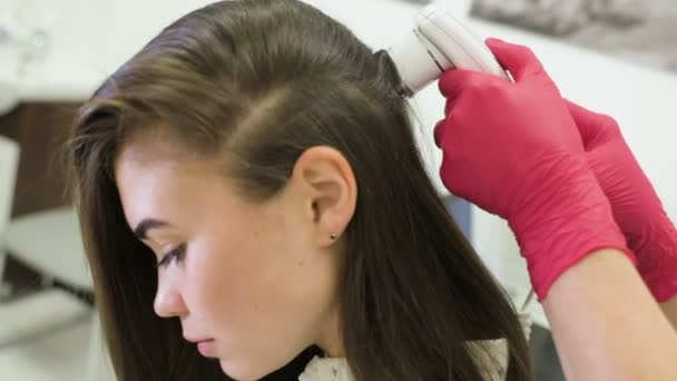 Dokter dermatoloog diagnoses de structuur van het haar van een jong mooi meisje met een speciaal hulpstuk - een trichoscope. — Stockvideo