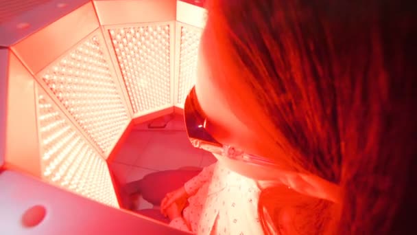 Das Mädchen durchläuft mit Hilfe einer Rotlichtbehandlung eine Hautverjüngung. — Stockvideo