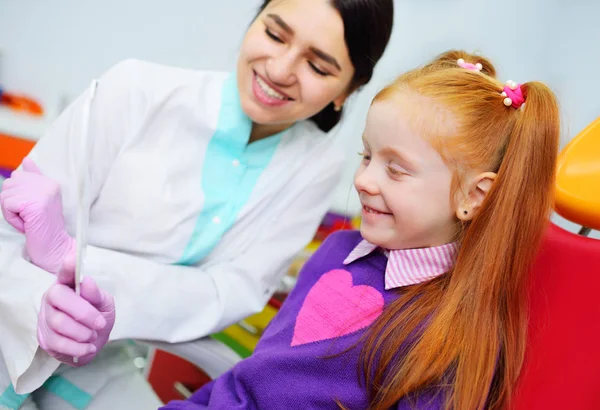 Dentista crianças examina os dentes e a boca da criança uma menina bonita ruiva sentada em uma cadeira dental — Fotografia de Stock