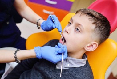 genç kadın diş hekimi diş sandalyede oturan bir erkek bebek diş inceliyor.