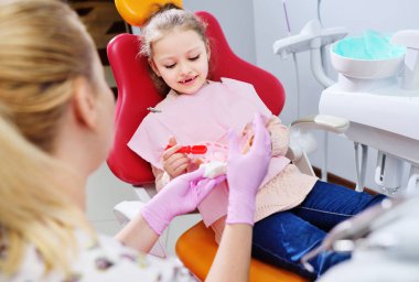 diş hekimi küçük kız bir yapay çene kukla üzerinde bir diş fırçası ile dişleri temizlemek nasıl gösterir.