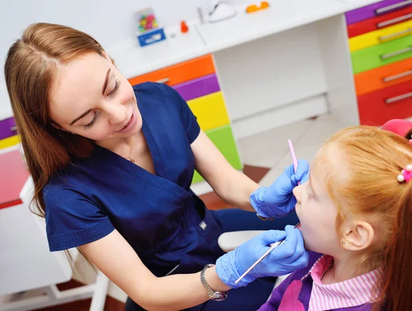 Dětský zubař zkoumá zuby a ústa dítěte - roztomilý rusovlasá dívka sedí v zubařském křesle — Stock fotografie