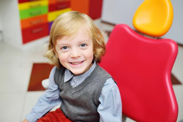 Retrato de uma criança sorridente com cabelo encaracolado loiro no exame em uma cadeira dentária . — Fotografia de Stock