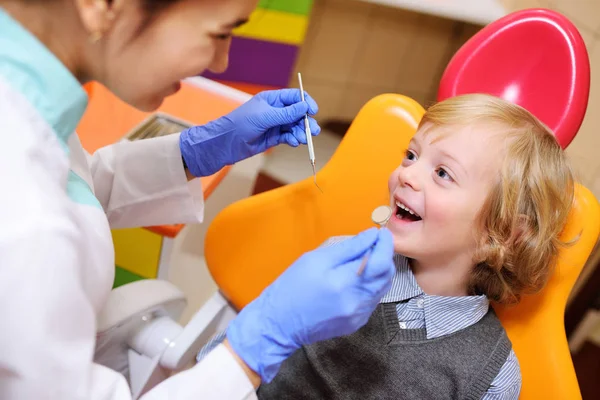 Niño sonriente con el pelo rubio rizado en la silla dental . — Foto de Stock
