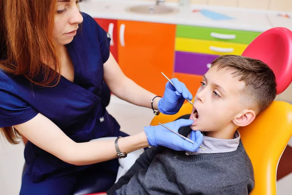 Dentista joven examina los dientes de un niño sentado en la silla dental . — Foto de Stock