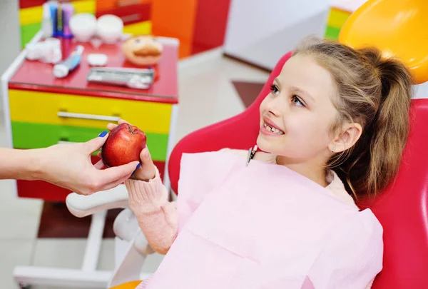 dentist gives ripe red Apple baby girl in the dental chair.