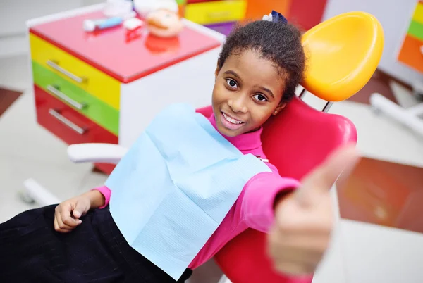 Leuke zwarte babymeisje glimlachend zitten in een rode tandheelkundige stoel — Stockfoto
