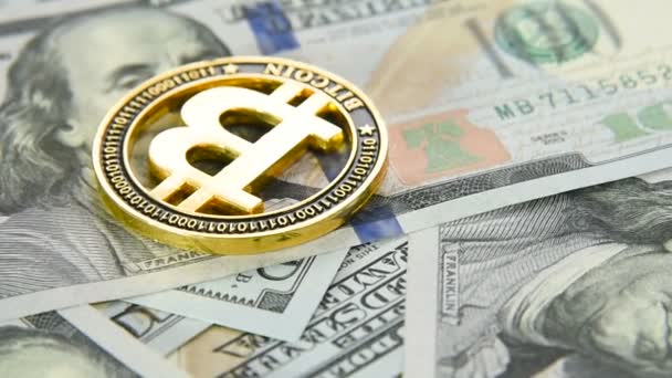 Gouden munten bitcoin sluiten - omhoog op de achtergrond van honderd dollarbiljetten van ons dollar. Rotatie. — Stockvideo