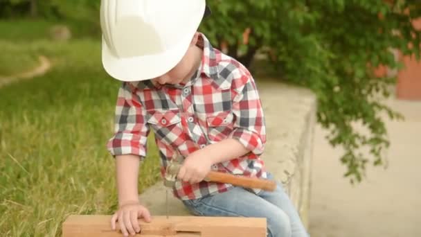 Menino em um capacete de edifício scoopes um prego — Vídeo de Stock