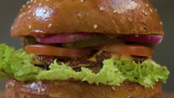 Hambúrguer suculento apetitoso com cebola, queijo, tomate, costeleta de carne em uma folha de salada close-up em um fundo cinza . — Vídeo de Stock