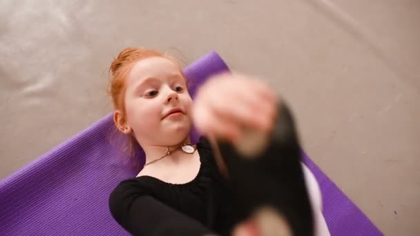 Little cute red-haired girl ballerina performs stretching exercises in ballet school on the background of a group of children — Stock Video
