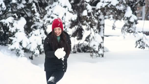 Joven linda chica sonriendo, divirtiéndose y arrojando nieve en el fondo del bosque de invierno y árboles cubiertos de nieve — Vídeo de stock