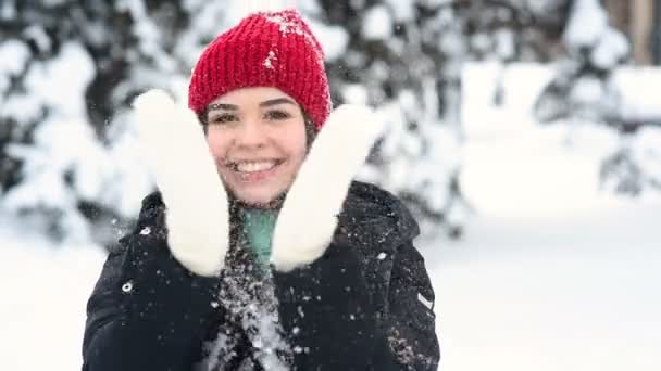 Joven linda chica sonriendo, divirtiéndose y arrojando nieve en el fondo del bosque de invierno y árboles cubiertos de nieve — Vídeo de stock