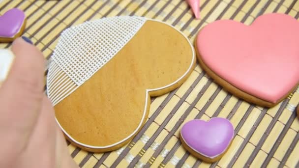 Mujer confitero decora y decora el esmalte con galletas de jengibre en forma de corazón . — Vídeos de Stock