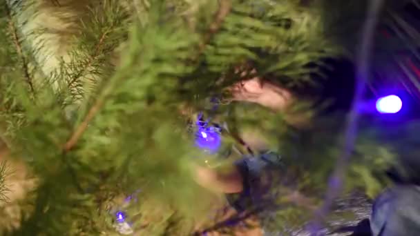 Niño acostado bajo el árbol de Navidad y colgar decoraciones de Navidad — Vídeos de Stock