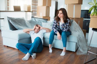 Çift taşındıktan sonra koltukta dinleniyor. Kanepede dinlenen kadın ve erkek yere karton kutularla taşınıyorlar. Yorgun ve üzgün ev sahipleri ve yeni evlerinin ilk günü.