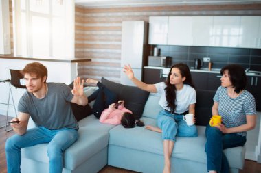 Büyük aile kanepede oturuyor. Bir eş ya da kız kardeş annemle konuşur ve kocalara ya da erkek kardeşlere seslenir. Dikkatinin dağılıp televizyon seyretmek istemiyor.