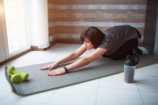 Vuxen passform smal kvinna har träning hemma. Senior modell sitter i asana poserar och sträcker ut sin kropp. Stark mogen kvinna sträcker ut sin kropp. — Stockfoto