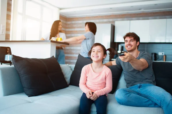 Velká rodina doma. Máma a dcera spolu komunikují. Otec nebo bratr se dívají na televizi. — Stock fotografie