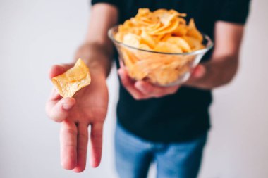 Genç adam bulanık arka planda izole edilmiş. Elinde patates cipsi olan adamın görüntüsünü kes. Adamın elinde bir parça var ve onu kamerada gösteriyor..