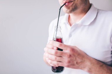Beyaz gömlekli genç adam arka planda izole edilmiş. Plastik kamışla kola içen adamın görüntüsünü kes. Şişeyi ellerimde tutuyorum..