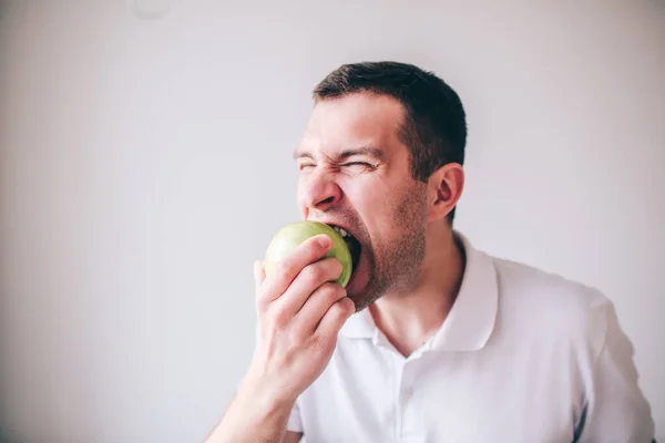 Arka planda izole edilmiş genç erkek gömleği. Taze, yeşil elmayı ısıran adam. Lezzetli meyveler..