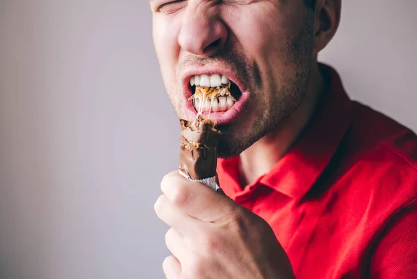 Young man in red shirt isolated over background. Close up of mouth opened for another portion of chocolate bar. Tasty delicious sweet yummy bar.