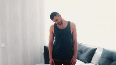 Genç adam evde egzersiz yapıyor. Adam oturma odasında durup egzersizden önce başını, boynunu ve ellerini ısıtıyor. Güçlü ve güçlü olmak için eğitim. Sabah aktivitesi.