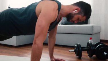 Genç adam evde egzersiz yapıyor. Kulaklıkla müzik dinlemek ve şınav çekmek. Güçlü ellerle hareket ediyor. Refah ve sağlık hizmetleri.
