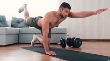 Genç adam evde egzersiz yapıyor. Yoga minderinde el ele tutuşun ve eğitim sırasında her seferinde bir lrg ve bir kol kaldırın. Güç ve güç kullanılıyor.