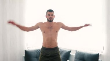 Genç adam evde egzersiz yapıyor. Güçlü kuvvetli bir adamın oturma odasında tek başına zıplayarak egzersiz yapması. Sağlığa dikkat et. Sağlık eğitimi..