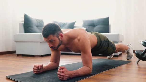 Junger Mann beim Training zu Hause. Video von kräftigem Kerl, der in Plankenstellung auf Yogamatte steht. Selbstbewusstes konzentriertes Mannschaftstraining im Wohnzimmer. — Stockvideo