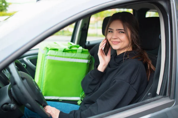 Conceito de entrega de alimentos. A mulher que entrega a comida tem uma mochila de geladeira verde. Ela se senta em um carro e entrega comida aos clientes — Fotografia de Stock