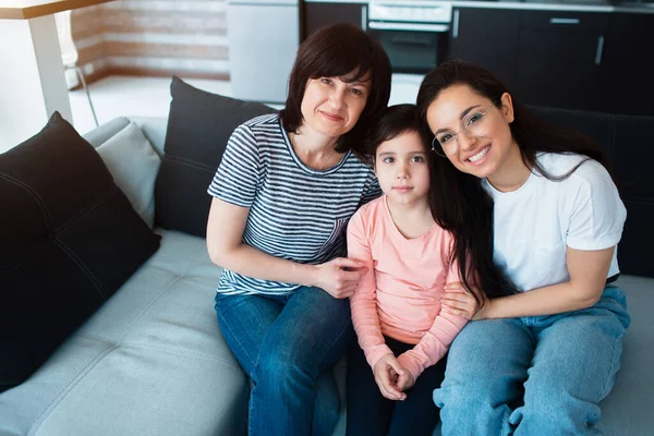 Šťastný rodinný portrét. Několik generací žen ze stejné rodiny se dívá do kamery. Příbuzní sedí doma na gauči. — Stock fotografie