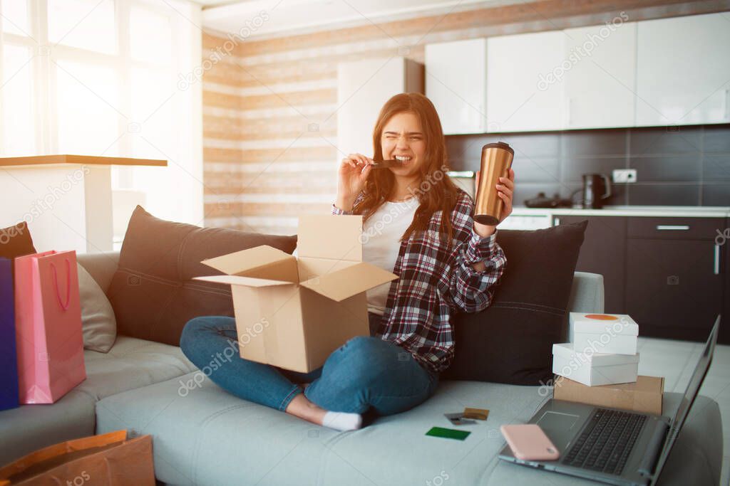 Shopping online, a young woman ordered home delivery. Now she sits on the couch and unpacks her new purchases.