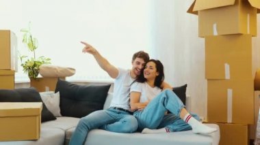 Genç çift yeni bir daireye taşınıyor. Güzel bir çift kanepede oturup eğleniyor. Adam öne bakıyor. Kamera arkaya doğru hareket ediyor. Apartman ve mobilya planları yapıyor..