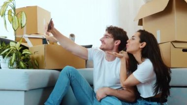 Genç çift yeni bir daireye taşınıyor. Neşeli adam ve kadın yerde oturup akıllı telefonların kamerasında poz veriyorlar. Selfie çekip komik yüz ifadeleri takınıyorum..