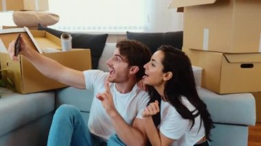 Genç çift yeni bir daireye taşınıyor. Kamera, yerde oturup selfie çeken insanlardan geriye doğru hareket ediyor. Komik yüz ifadeleri ve poz vermek. Taşındıktan sonra mutlu insanlar..