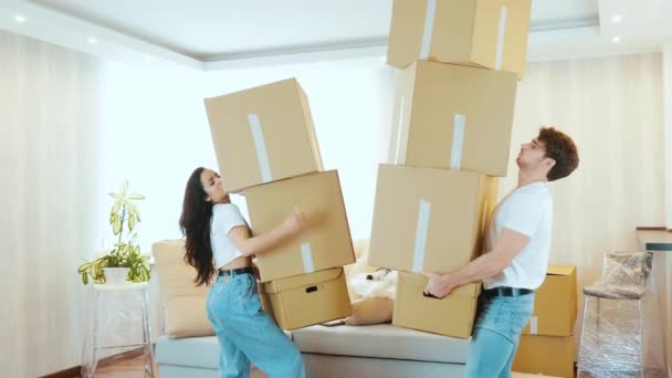 Una pareja joven se muda a un apartamento nuevo. El hombre y la mujer llevan cajas grandes una sobre otra y tratan de equilibrarlas. Una caja cayéndose. chico molesto tirarlos en el suelo y alejarse . — Vídeos de Stock