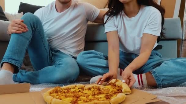 Un jeune couple emménage dans un nouvel appartement. Asseyez-vous par terre et mangez de la pizza. Célébration du déménagement dans un nouvel appartement. Manger en même temps. — Video