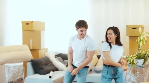 Ungt par flytter ind i en ny lejlighed. Stå midt i deres lejlighed og dans sammen. Slå hinanden røv og have det sjovt. Par spiller og afslappende. – Stock-video