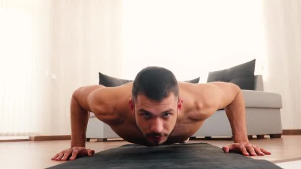 Ο νεαρός γυμνάζεται στο σπίτι. Μπροστά όψη του δυνατού σέξι ισχυρό άντρα κάνει push ups μπροστά κάμερα. Κοίτα μπροστά κατά τη διάρκεια της άσκησης. Άσκηση στο σαλόνι. — Αρχείο Βίντεο